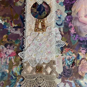 May include: A decorative, handmade piece featuring a cream-colored base adorned with lace, floral embellishments, and a jeweled letter "A". The design incorporates vintage-style imagery and a variety of textures, creating a layered, artistic aesthetic.
