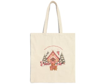 Puede incluir: Una bolsa de tela beige con una ilustración impresa de una casa de jengibre rosa rodeada de pinos nevados y tres figuras de jengibre. El texto "Winter Wishes and Gingerbread Kisses" está impreso en color rojo sobre la casa.
