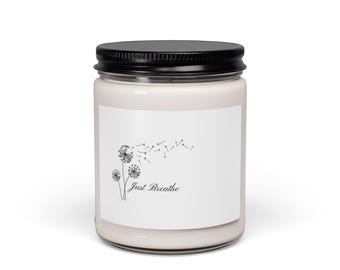 Puede incluir: Un frasco de vela de vidrio transparente lleno de cera de color claro, cubierto con una tapa negra de rosca. La etiqueta blanca presenta un dibujo lineal negro de tres dientes de león con semillas al viento y el texto Just Breathe.