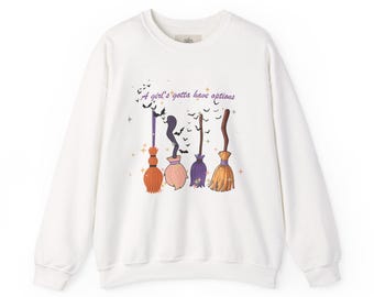 Puede incluir: Una sudadera blanca de manga larga con un estampado gráfico de cuatro escobas de diferentes colores y el texto A girl's gotta have options escrito encima. El diseño incluye pequeños murciélagos negros y estrellas naranjas alrededor.