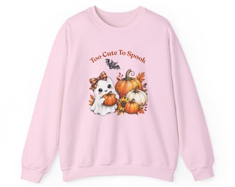Puede incluir: Una sudadera de cuello redondo rosa claro con un gráfico de un fantasma blanco con un lazo a cuadros, sosteniendo una calabaza, rodeado de hojas de otoño, girasoles, calabazas y un pequeño murciélago.