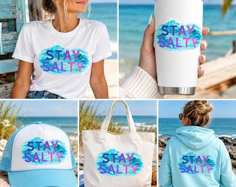 Puede incluir: Una camiseta blanca, un vaso de acero inoxidable blanco, una gorra de camionero azul claro y blanca, una bolsa de tela y una sudadera con capucha azul claro, cada una con un gráfico de ola en acuarela azul y el texto morado STAY SALTY.