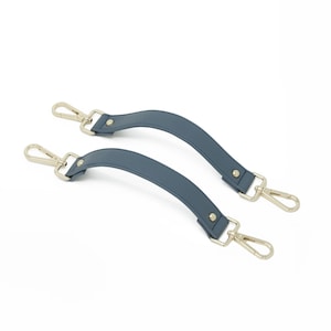 May include: Two blue-grey purse handles with silver-colored metal clasps. The handles are curved and secured with small silver rivets. The clasps are designed to attach to a bag.