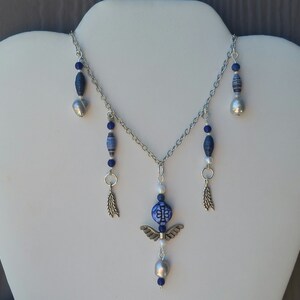 May include: A silver chain necklace with blue and white beads, a silver angel charm, and silver feather charms.
