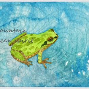 May include: A watercolor painting of a green frog on a blue background with the words "mountain ocean spirit" written in cursive.