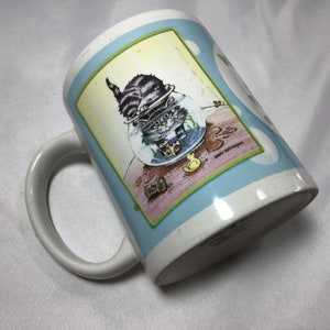 Op de afbeelding: Een witte keramische mok met een blauw en groen ontwerp. Het ontwerp toont een kat in een viskom met een geel rubberen eendje. De tekst "When in doubt, just meow" staat op de mok.