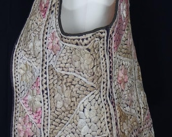 May include: An ornate, sleeveless vest with intricate floral embroidery. The vest features a cream-colored background with pink and beige floral patterns, outlined with dark brown trim. The design is detailed and appears to be hand-stitched.
