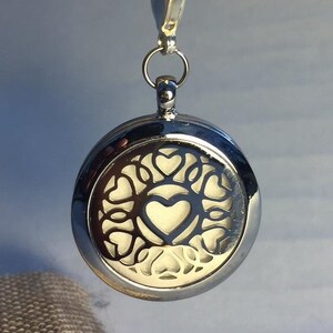 Puede incluir: Llavero plateado con un dije redondo plateado que presenta un diseño de corazón con un patrón de corazones recortados.