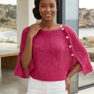 May include: A magenta-colored, knitted poncho with three large, round, white buttons on the right shoulder. The poncho has a boat neck and short sleeves. The person is wearing white pants.