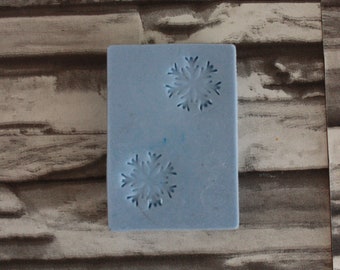 May include: A light blue rectangular mold with two snowflake designs. The mold is made of a flexible material and is likely used for crafting or baking. The snowflakes are detailed and evenly spaced.