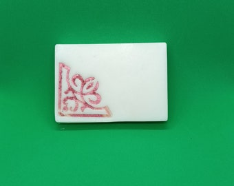 May include: A white rectangular soap bar with a pink floral design in the corner.