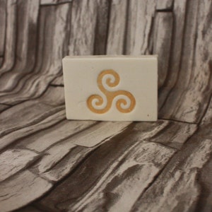 May include: A white bar of soap with a yellow triskelion symbol on the top.