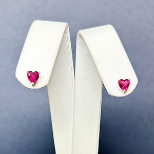 May include: A pair of heart-shaped earrings with pink gemstones set in gold.
