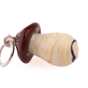 Op de afbeelding: Een paddenstoelvormige bedel met een zilveren ring. De bovenkant is glanzend donkerbruin, de steel is cr&egrave;mewit met bruine marmering en een zwarte spiraal. Voor ketting of armband. Afmetingen in centimeters.