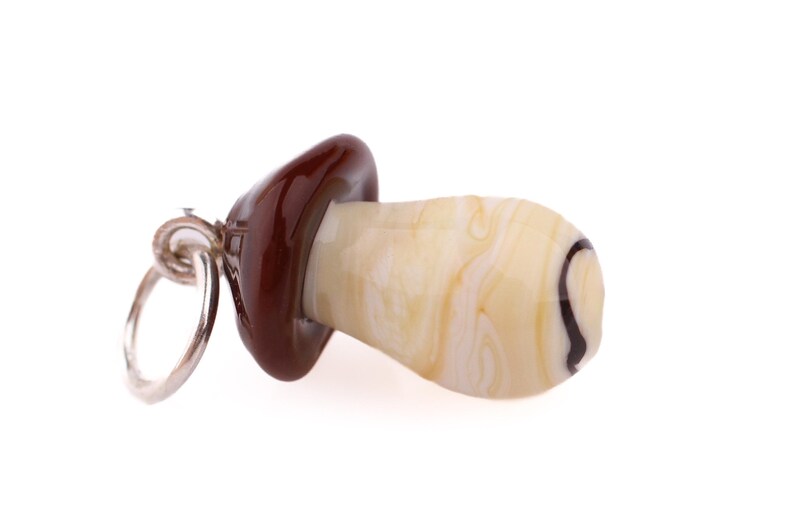 Op de afbeelding: Een paddenstoelvormige bedel met een zilveren ring. De bovenkant is glanzend donkerbruin, de steel is cr&egrave;mewit met bruine marmering en een zwarte spiraal. Voor ketting of armband. Afmetingen in centimeters.