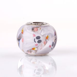Op de afbeelding: Een heldere glazen kralenbedel met een wit spookontwerp en roze en oranje candy corn accenten. De kraal is voor een bedelarmband.