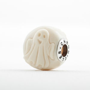 May include: White ceramic bead featuring a carved ghost design. The bead has a silver metal charm with the word "CHRONICLE" engraved on it.