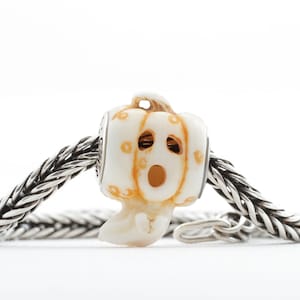 May include: A white ceramic pumpkin bead with orange details and a carved face, on a silver chain bracelet.