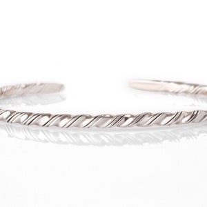 May include: A silver twisted bangle bracelet. The bracelet is made of a single piece of metal that is twisted into a rope-like design.