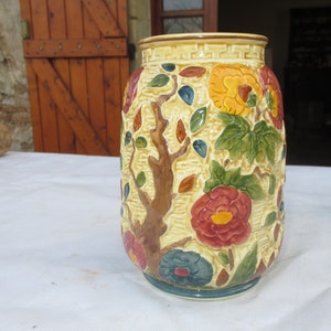May include: A ceramic vase with a floral design. The vase is decorated with a tree, flowers, and leaves in shades of brown, yellow, red, green, and blue.