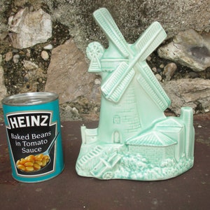 Könnte beinhalten: Eine Keramik-Windmühlenfigur in hellgrüner Glasur. Die Windmühle hat ein weißes Dach und einen braunen Sockel. Die Figur steht auf einer braunen Oberfläche.