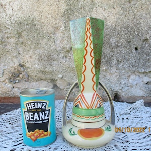 May include: A vintage ceramic vase with a geometric design in shades of green, orange, and white. The vase has a tall, slender neck and a wide, round base. It features a silver-coloured handle on each side.