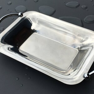 May include: A silver serving tray with two handles. The tray is rectangular and has a shiny, reflective surface.