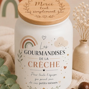 Peut inclure: Un bocal en céramique blanche avec un couvercle en bois gravé Merci tout simplement. Le corps du bocal présente un arc-en-ciel, un nuage et le texte Les GOURMANDISES DE LA CRÈCHE, suivi de Pour toute l'équipe qui prend soin de nos petits trésors.