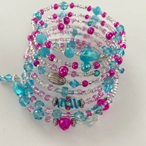 Könnte beinhalten: Ein mehrreihiges Armband aus silbernen, rosa und blauen Perlen. Das Armband ist um sich selbst gewickelt, um einen dicken, geschichteten Look zu erzeugen.