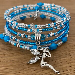 May include: A multi-strand bracelet with blue and clear beads, a silver fairy charm, and a silver star charm.