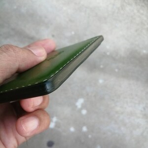 Puede incluir: Una cartera de cuero verde con un borde cosido.