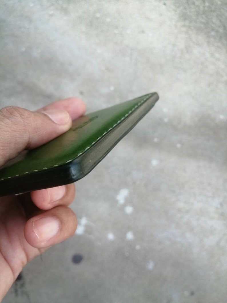 Puede incluir: Una cartera de cuero verde con un borde cosido.