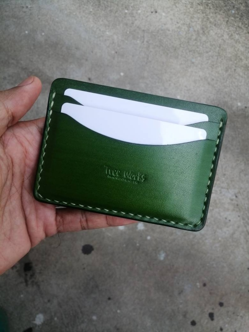 Puede incluir: Un porta tarjetas de cuero verde con costuras blancas y el texto "The Works" en relieve en la parte delantera.