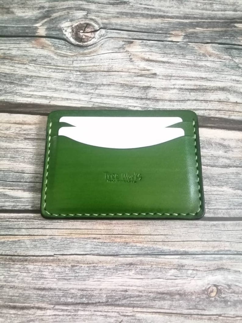 Puede incluir: Un porta tarjetas de cuero verde con un borde cosido y el texto "Tree Works" en relieve en la parte delantera.