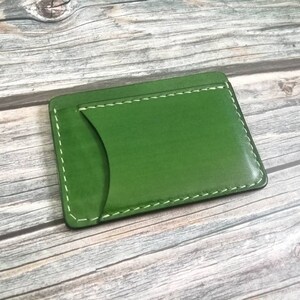 Puede incluir: Un porta tarjetas de cuero verde con costuras blancas. El porta tarjetas tiene un solo bolsillo para tarjetas.