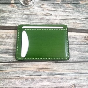 Puede incluir: Un porta tarjetas de cuero verde con interior blanco y costuras blancas alrededor de los bordes.