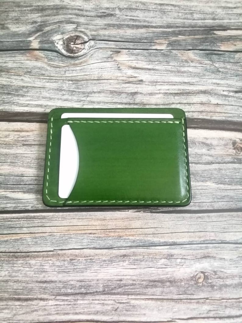 Puede incluir: Un porta tarjetas de cuero verde con interior blanco y costuras blancas alrededor de los bordes.