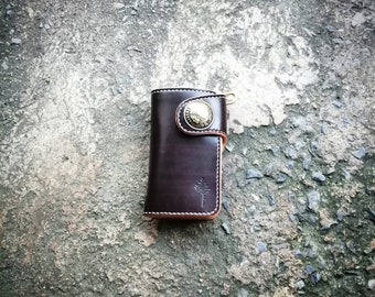 May include: A brown leather wallet with a metal button closure and a small tree logo. The wallet has a light brown stitching detail and a key ring.