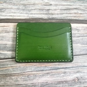 Puede incluir: Un porta tarjetas de cuero verde con un borde cosido y el texto "True Wallets" en relieve en la parte delantera.