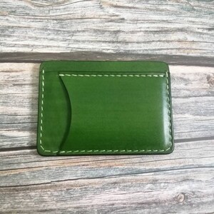 Puede incluir: Una cartera de cuero verde con una sola ranura para tarjeta y costuras blancas.