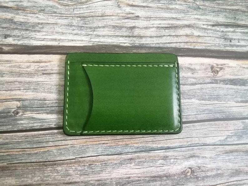 Puede incluir: Una cartera de cuero verde con una sola ranura para tarjeta y costuras blancas.