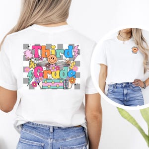 May include: White t-shirt with a colorful "Third Grade" graphic on the back, featuring a smiley face, flowers, and a pencil. A smaller image on the right shows a smiley face with text. The shirt is paired with blue jeans.