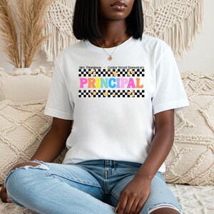 May include: White t-shirt with the word "PRINCIPAL" in colorful letters. The shirt also features the text "Mrs. Thompson Center Street Elementary" above the word "PRINCIPAL". The design includes a black and white checkered pattern.