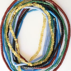 May include: A collection of colorful glass beads in various shades of blue, green, yellow, and brown. The beads are arranged in a circular pattern, creating a visually appealing display.