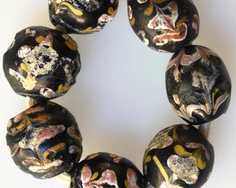 May include: A strand of black glass beads with intricate gold and pink floral patterns. The beads are strung on a white cord.