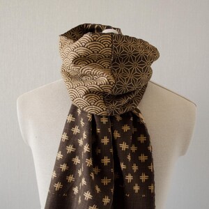 Puede incluir: Una bufanda marrón con un patrón geométrico en beige. La bufanda está hecha de un tejido suave y tejido y tiene un borde con flecos.