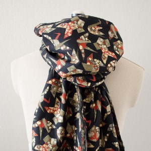May include: A black scarf with a fringed edge features a repeating pattern of origami cranes in gold, red, and green on a black background.