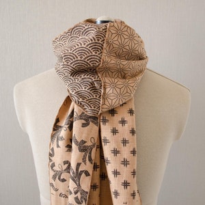 May include: A brown scarf with a geometric pattern. The scarf is made of a soft, woven fabric and has a fringed edge.