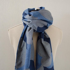 May include: A blue and gray patterned scarf with a fringed edge. The scarf is draped around a mannequin's neck.