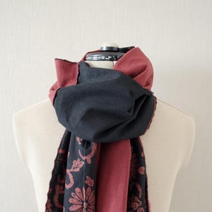 May include: A reversible scarf with a black side and a burgundy side. The burgundy side has a floral pattern in a darker shade of burgundy.